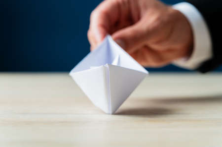Hand of a businessman holding white origami paper boat sailing towards you in a conceptual image.の写真素材