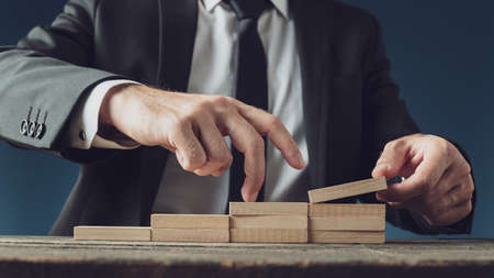 Businessman assembling stairway of wooden pegs as he walks his fingers upwards in a conceptual image.の写真素材