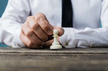 Closeup of businessman placing white pawn chess piece on rustic wooden desk in a conceptual image.の写真素材