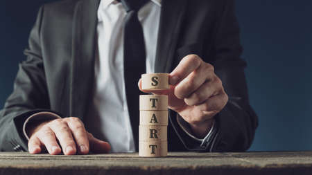 Businessman stacking wooden cut circles to assemble the word Start in a conceptual image.