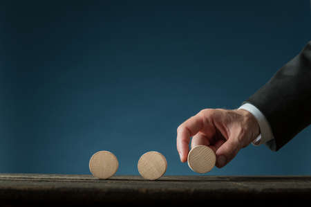 Hand of a businessman placing three blank wooden cut circles in a row over blue background. With copy space.の写真素材