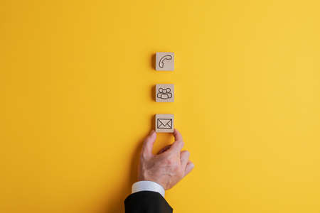 Businessman placing three wooden blocks with contact and communication icons on them on a bright...