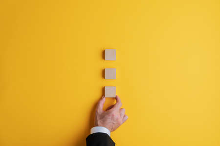 Hand of a businessman placing three blank wooden blocks on bright yellow background.の写真素材