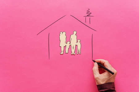 Male hand drawing a house shape around a paper cut family silhouette of five in a conceptual image of safety and shelter. Over pink background.の写真素材