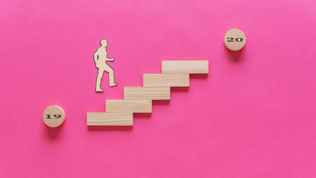 Paper cut silhouette of a man walking up the stairs made of wooden pegs from the year 2019 towards...