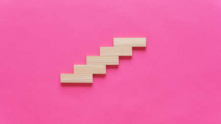 Blank wooden pegs placed in a stairway like structure in a conceptual image. Over pink background with copy space.の写真素材