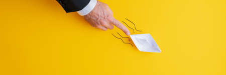 Wide view image of businessman pushing paper made origami boat forward in a conceptual image. Over yellow background with copy space.の写真素材