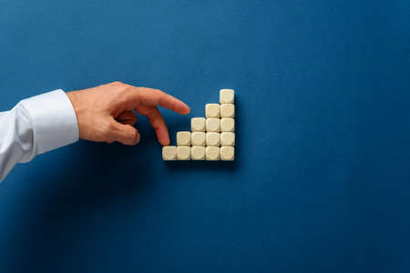 Businessman walking his fingers up the stairs made of wooden dices in a conceptual image. Over blue...