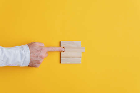 Businessman pushing the second peg from the top out of the stack of them in a conceptual image. Over yellow background.の写真素材