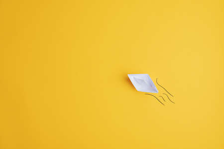 White paper made origami boat on yellow surface with hand drawn waves behind it. With copy space ready for your message or text.の写真素材