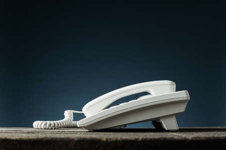 Low angle view image of white landline telephone on rustic wooden desk. Over blue background with...