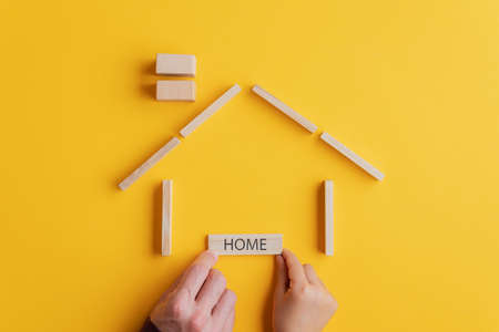 Father and son placing a wooden Home tag under a house made of pegs and blocks in a conceptual image. Over yellow background.の写真素材