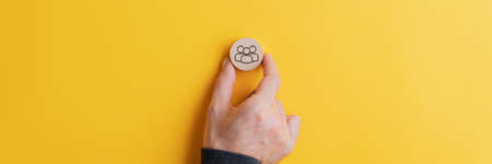 Male hand placing wooden cut circle with people symbol on it on bright yellow background. Wide view...