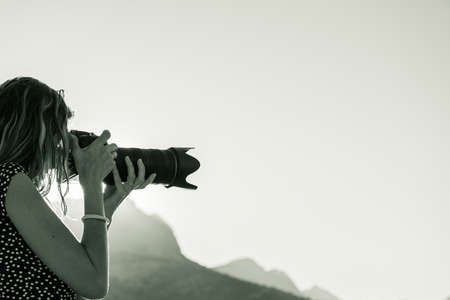 Monochrome image of a young woman taking a photo with dslr camera outside at sunrise.の写真素材