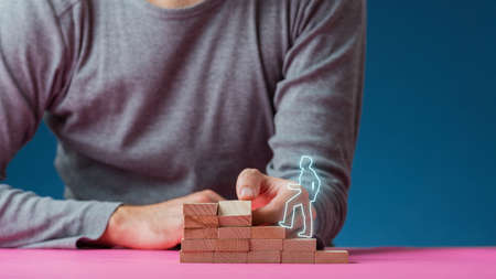 Man making steps of wooden pegs for a glowing shape of a man walking upwards in a conceptual image.