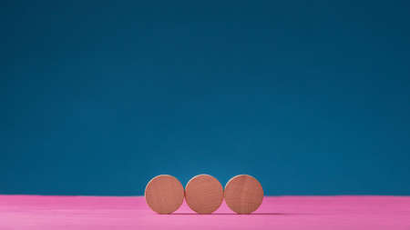 Three blank wooden cut circles placed in a row on pink surface over blue background.の写真素材