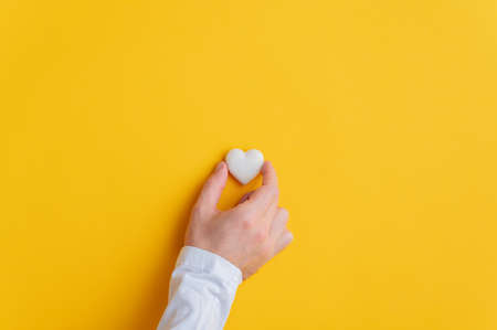 Male hand placing a marble heart over yellow background. With plenty of copy space.の写真素材
