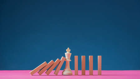 King chess figure standing in the middle of falling dominos to prevent them from collapsing...