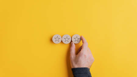 Male hand placing three wooden cut circles with star shape on them in a row over yellow background....
