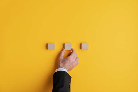 Hand of a businessman placing three wooden blocks in a row over yellow background. With copy space.