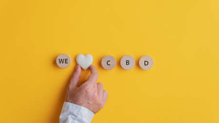 Male hand making a We love CBD sign spelled on wooden cut circles with heart shaped marble in the middle. Over yellow background with copy space.の写真素材