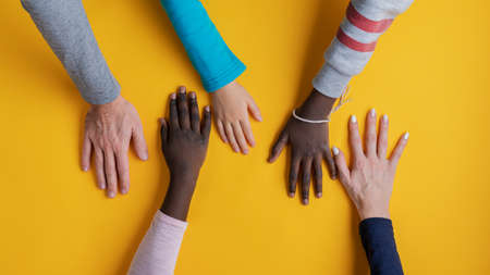 Five hands of a mixed race family placed over yellow background.の写真素材