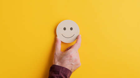 Male hand placing a wooden cut circle with smiling face on it on yellow background. With copy space.の写真素材
