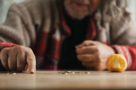 Low angle view of senior homeless man counting coins with a bitten apple on a desk.の写真素材