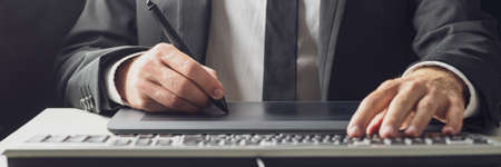 Wide view image of businessman or graphic designer using a stylus pen and tablet while typing on his...