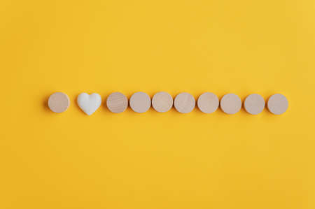 Nine blank wooden cut circles placed in a row with heart shaped marble in between. Ready for your own text or message. Over yellow background.の写真素材