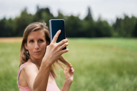 Young woman making selfies with her smart phone outside in nature.