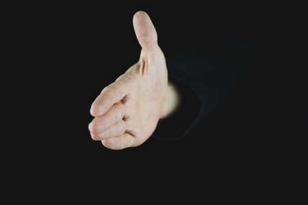 Hand of a businessman offering a handshake coming out of black background.の写真素材