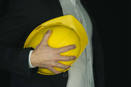 Closeup view of contractor in a suit holding bright yellow protective workwear helmet.
