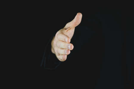 Hand of a businessman coming out of a black background offering a handshake.の写真素材