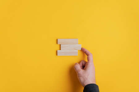 Male hand stacking three wooden pegs in a conceptual image. Over yellow background with copy space.
