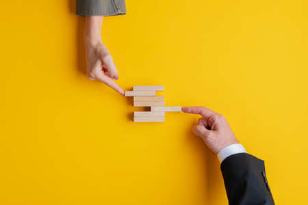 Business teamwork and cooperation concept - hands of businessman and businesswoman pushing wooden peg in a stack of them. Over yellow background, with copy space. の写真素材