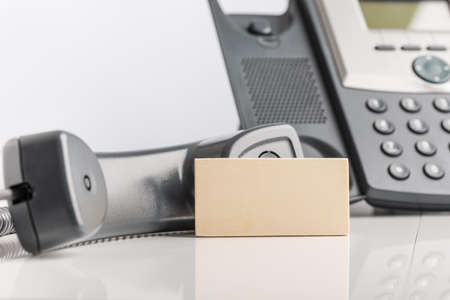 Blank business card leaning on black landline telephone in conceptual image.