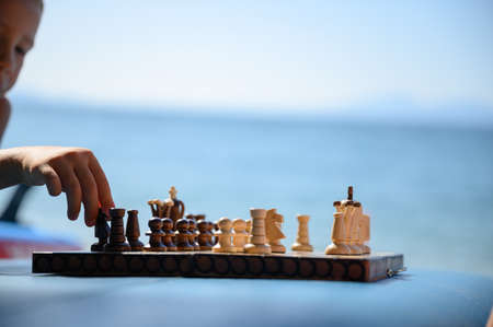 Little boy playing chess on sup board on the beach with ocean in background.