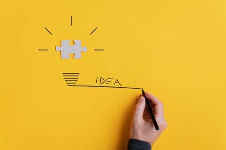 Male hand drawing light bulb with the word idea to the side. Over yellow background.の写真素材