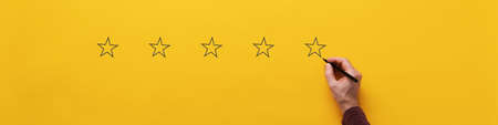 Wide view image of male hand drawing five stars over yellow background.の写真素材