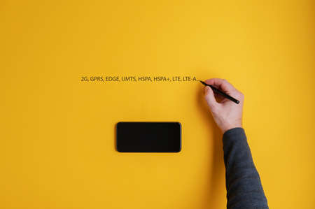 Black mobile phone placed over yellow background with male hand writing various mobile network...