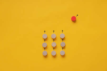 Group of blank wooden cut circles turned in the same direction and a red one going its own way. Conceptual image of standing out of the crow and uniqueness.の写真素材