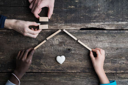 Mixed family building a house of wooden blocks over rustic wooden background. Conceptual image of...