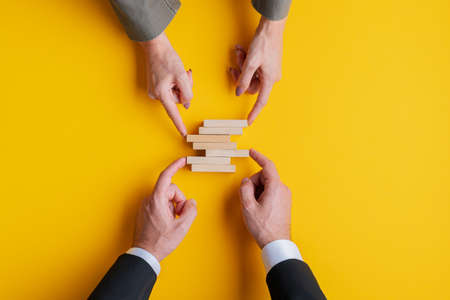 Business teamwork conceptual image - hands of a businessman and businesswoman making a stack of blank wooden pegs. Over yellow background.の写真素材