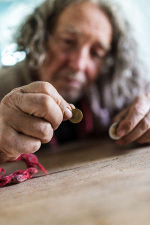Conceptual image of poverty and personal crisis - senior man in torn sweater counting Euro coins.