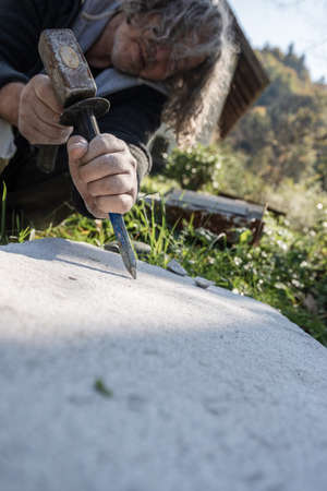 Low angle view of a senior artist carving in block of stone with chisel and a mallet.の写真素材
