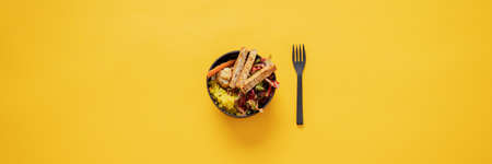 Wide view image of delicious vegan Buddha bowl meal served in coconut bowl with fork next to it. Over yellow background with copy space.の写真素材