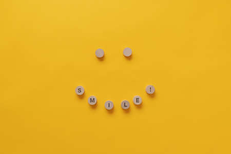 Smiling face made of wooden cut circles with Smile! sign on them in a conceptual image. Over yellow background with copy space.の写真素材