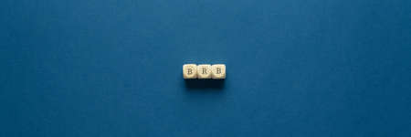 Wide view image of BRB abbreviation spelled on wooden dices. Placed over navy blue background.の写真素材