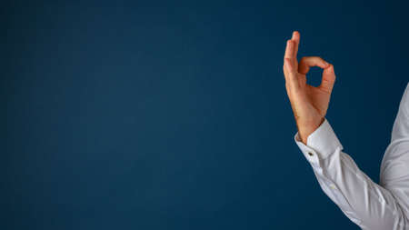 Hand of a businessman showing an ok gesture with his fingers. Over blue background with plenty of copy space on the left side of an image.の写真素材